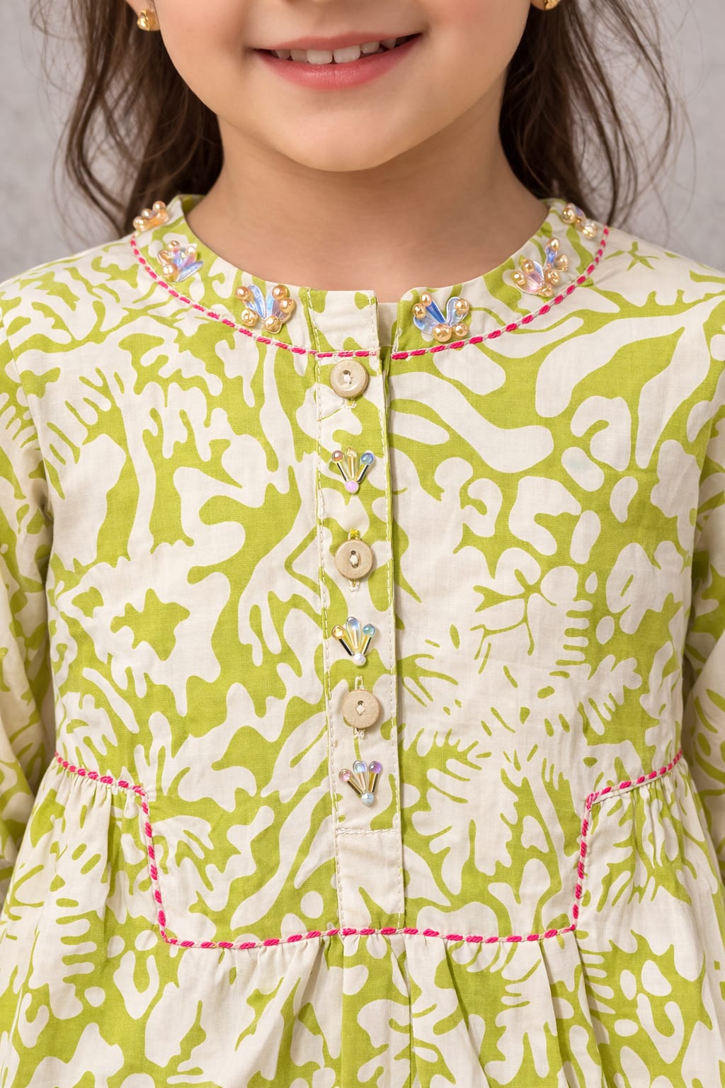 Close-up of a child wearing a green and white patterned dress with decorative buttons and trim.
