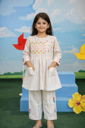 Young girl in a white outfit with colorful patterns standing in front of a colorful backdrop.